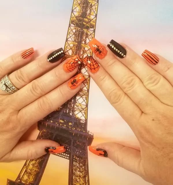 Client’s orange and black Halloween nail art held up in front of an Eiffel Tower picture