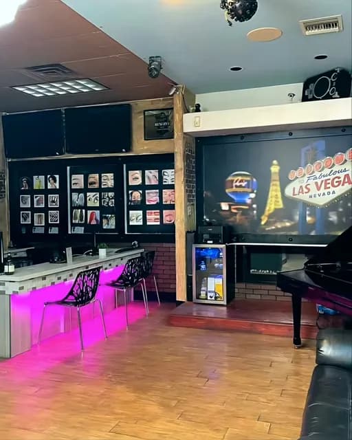 Lounge corner with pink under-lit seating, a Welcome to Las Vegas mural and a piano