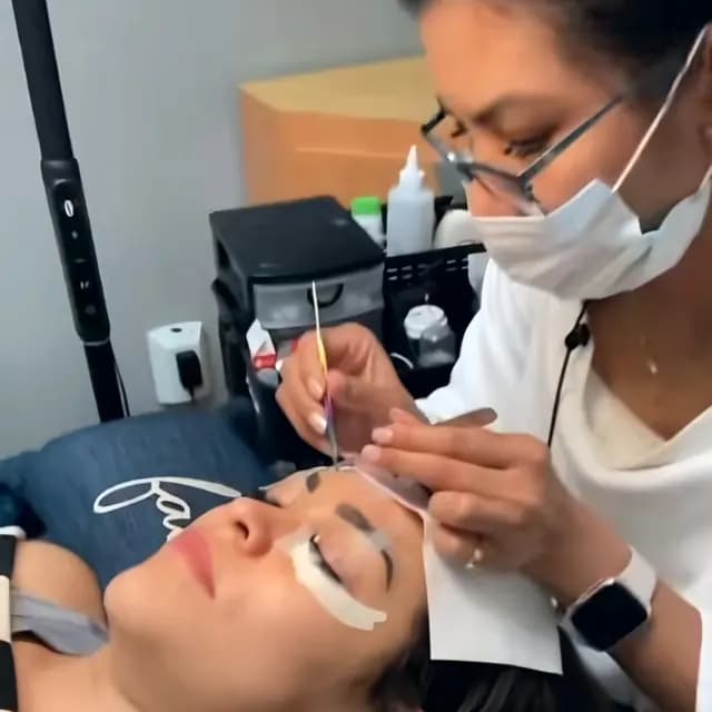 Masked lash artist applying extensions to a client in the lash room