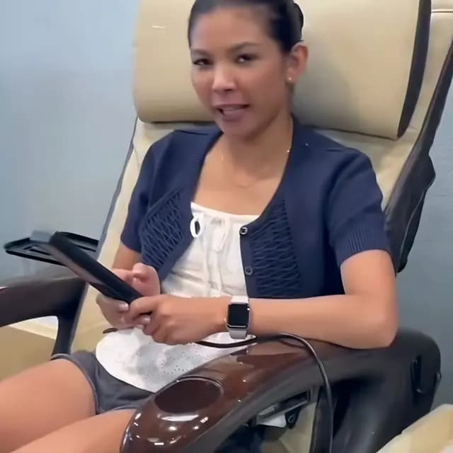 Client relaxing in a cream pedicure chair, scrolling her phone