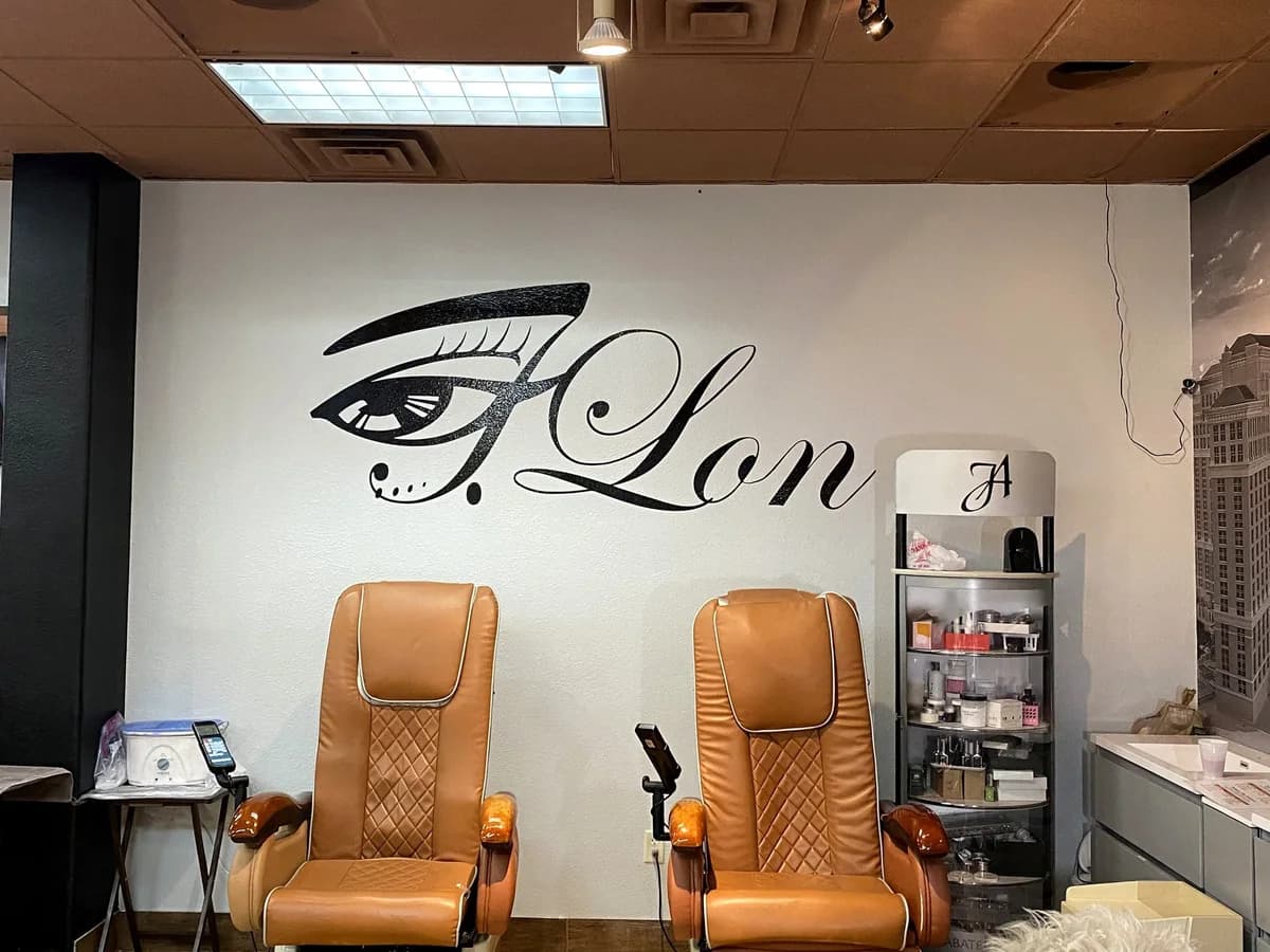 Two tan pedicure chairs in front of the JLon logo wall